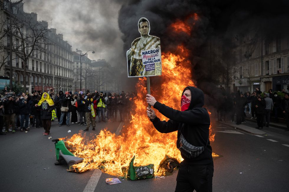 Man with sign of Emmanuel Macron stands in front of a fire