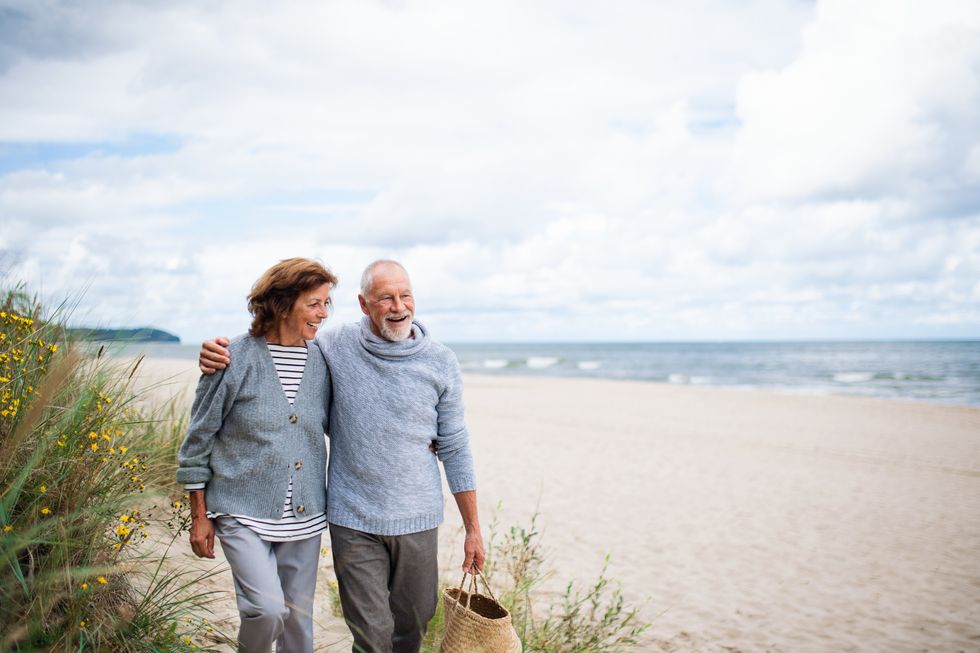Mature couple walk along beach smiling