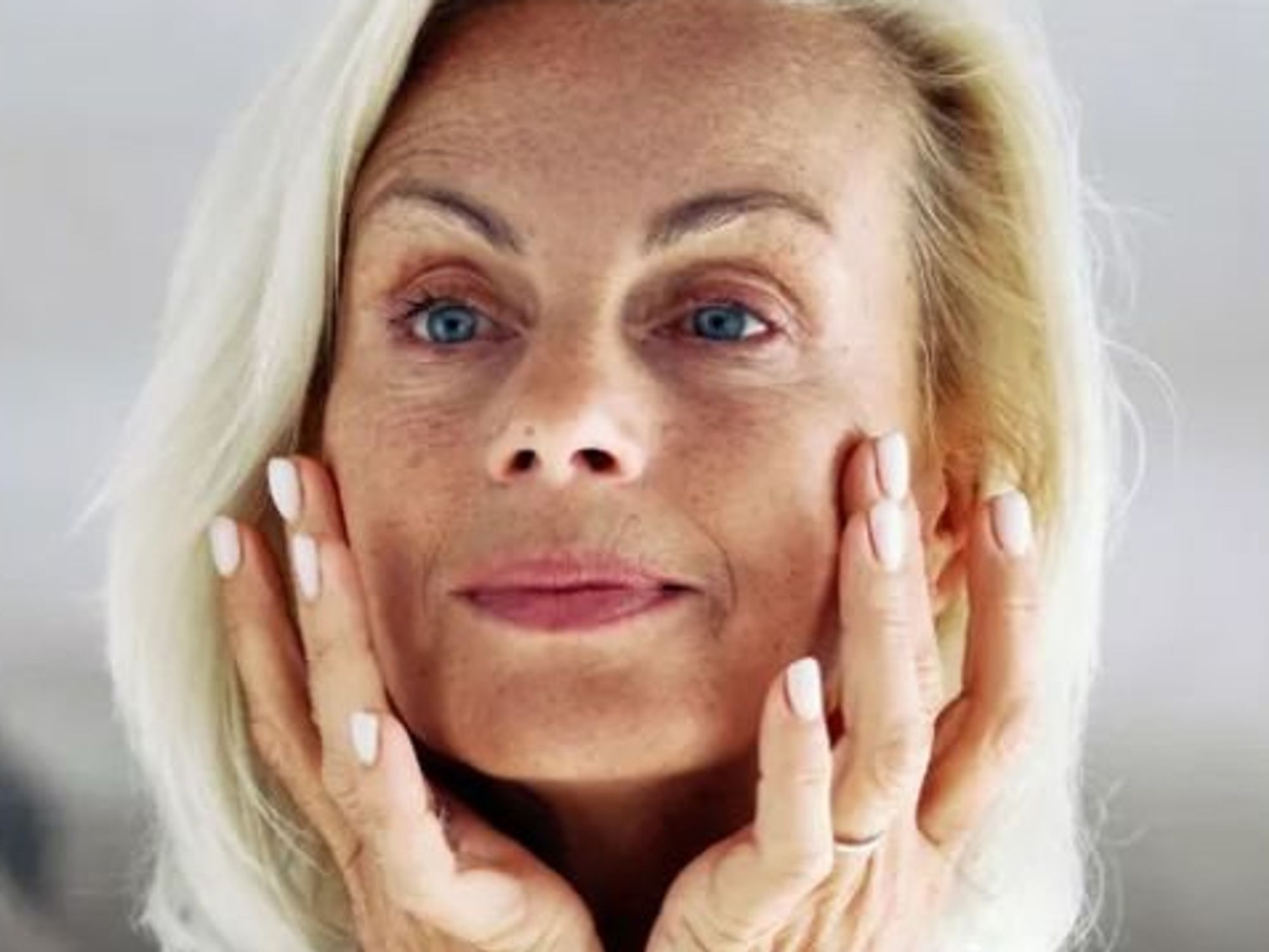 Mature woman checking lines around eyes / Mature woman examining face in mirror
