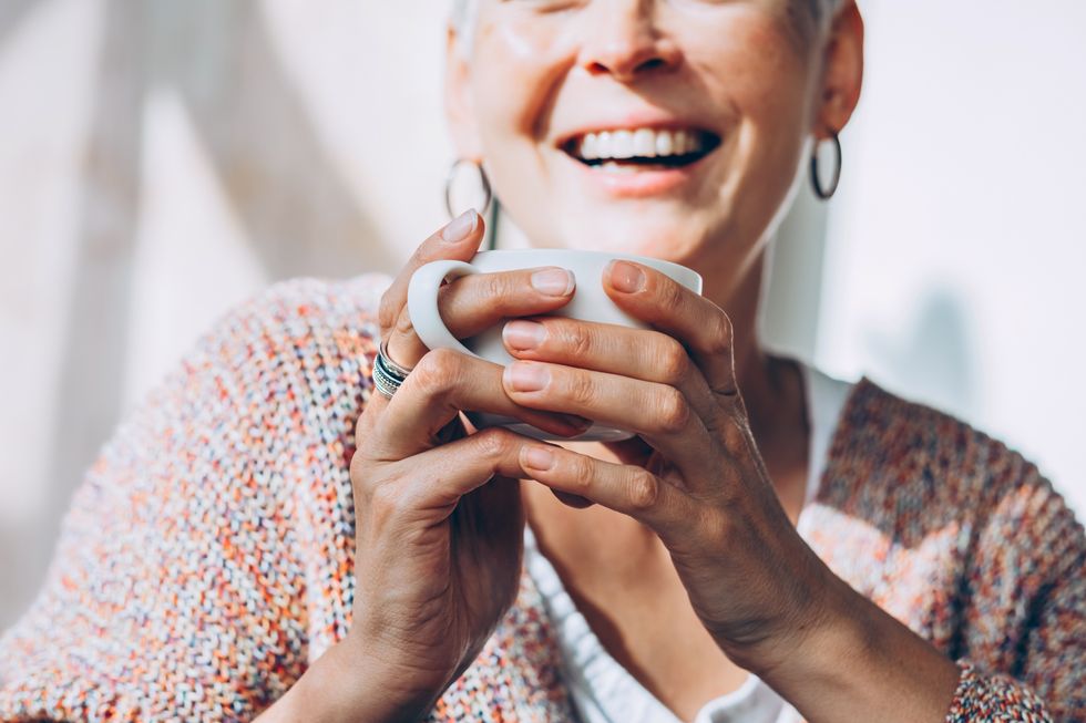 Mature woman holding a white cup of coffee smiling