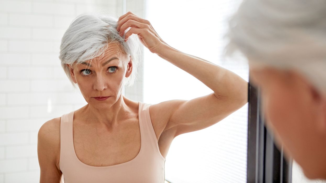 Mature woman looking at her grey hair in mirror