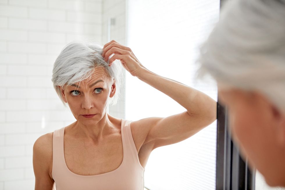 Mature woman looking at her grey hair in mirror