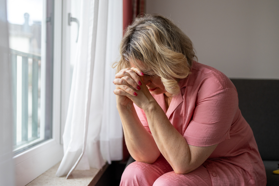 Mature woman with her head in her hands by a window