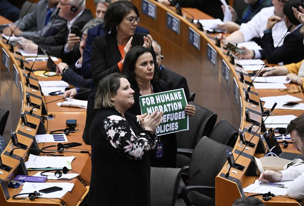 Members of Parliament react by holding a sign reading "for humane migration"