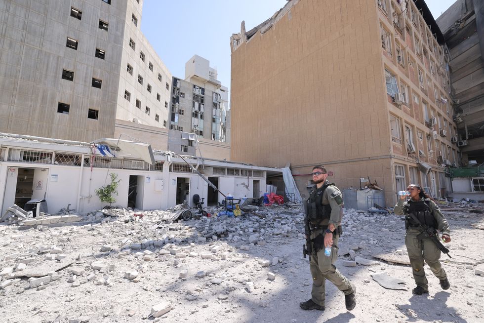 Members of the Israeli security forces walk at the Soroka Medical Center, the city's general hospital, at an impact site following a missile strike from Iran on Israel, in Beersheba