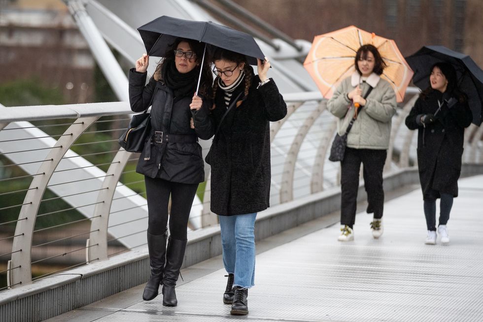 Members of the public cross Millennium Bridge in wet and windy weather in London.
