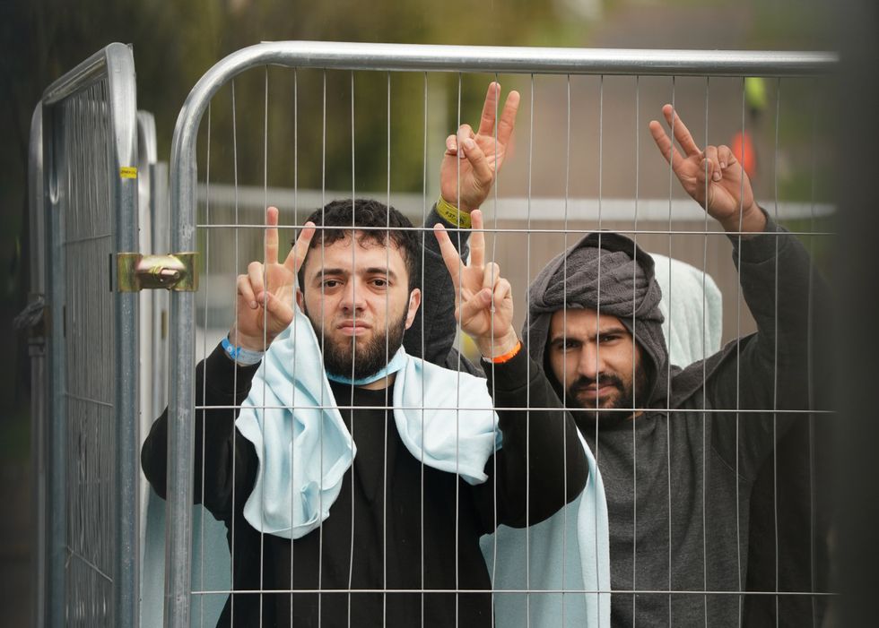 Men thought to be a migrants gesture towards members of the media at the Manston immigration short-term holding facility located at the former Defence Fire Training and Development Centre in Thanet, Kent.