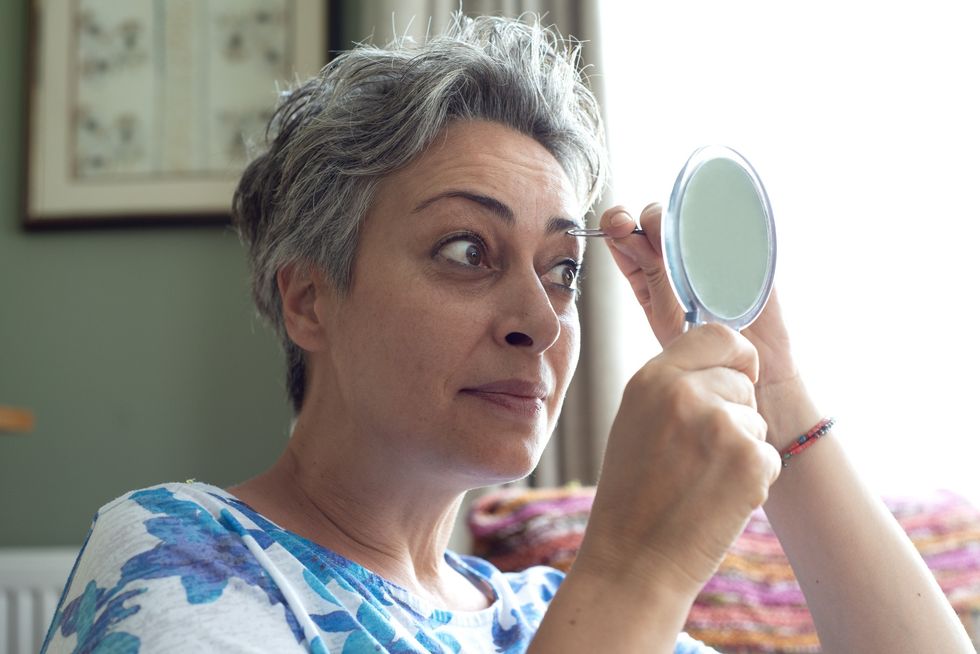 Middle-aged woman plucking her eyebrows