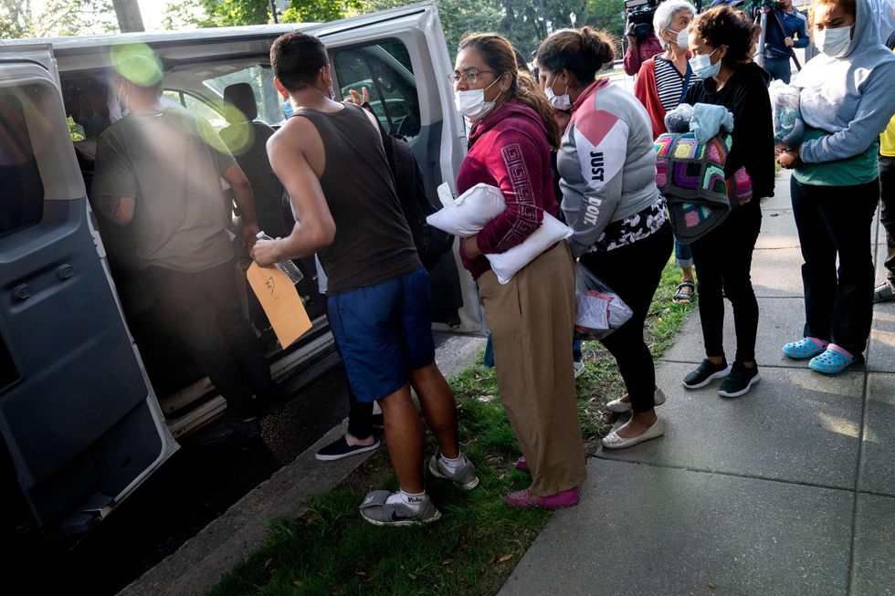 Migrants from Venezuela, who boarded a bus in Texas, wait to be transported to a local church by volunteers after being dropped off outside the residence of US Vice President Kamala Harris