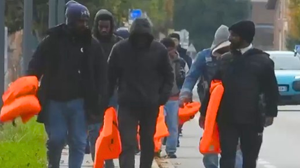 Migrants holding flotation aids walk through a French street