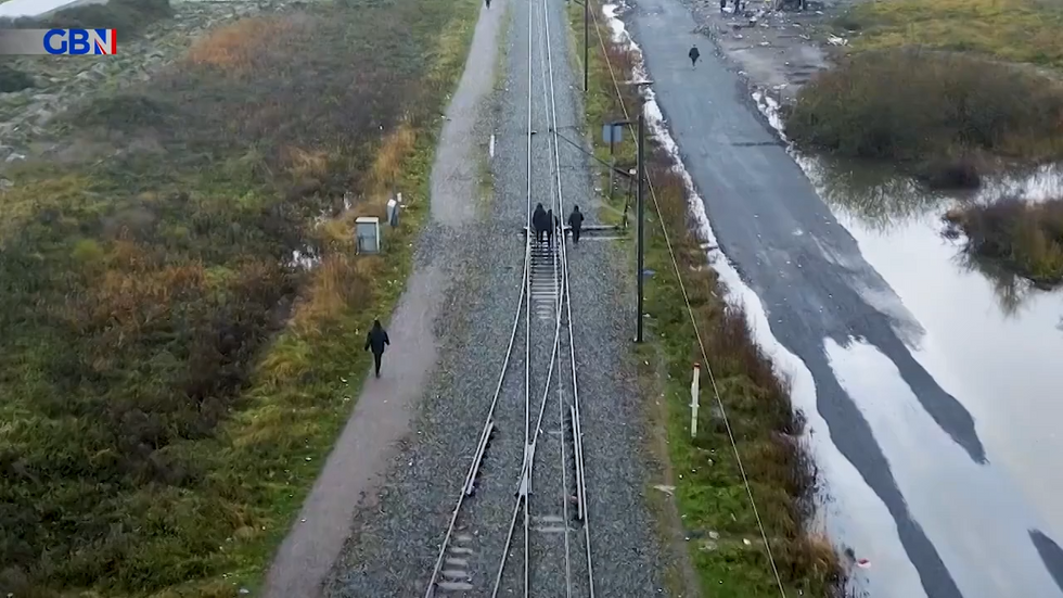 Migrants walk down train track