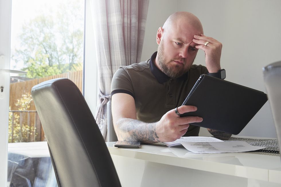 Mortgage holder looks worried at tablet and paperwork