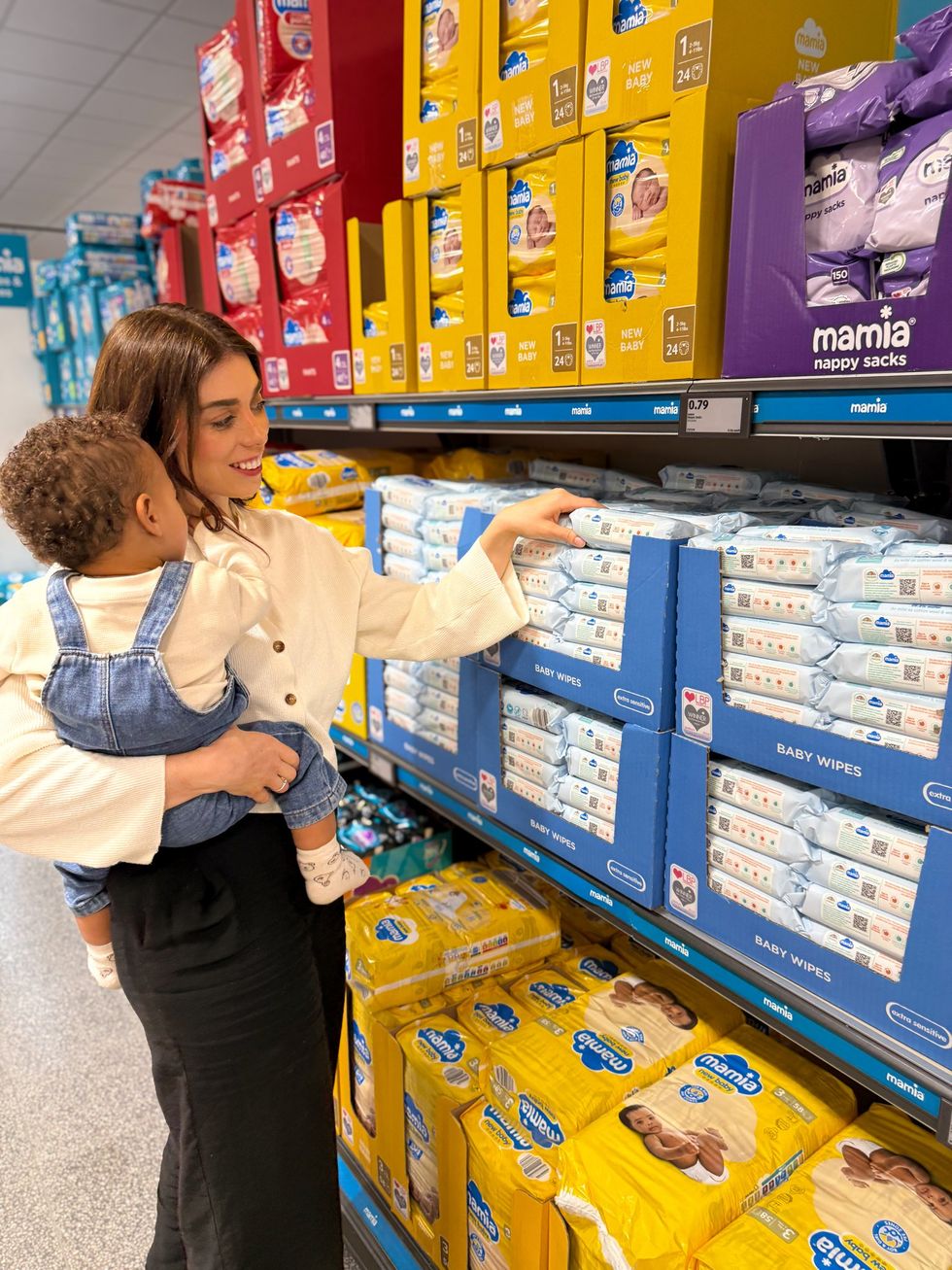 Mum holding baby in Aldi, picking up Mamia x PANDAS baby wipes