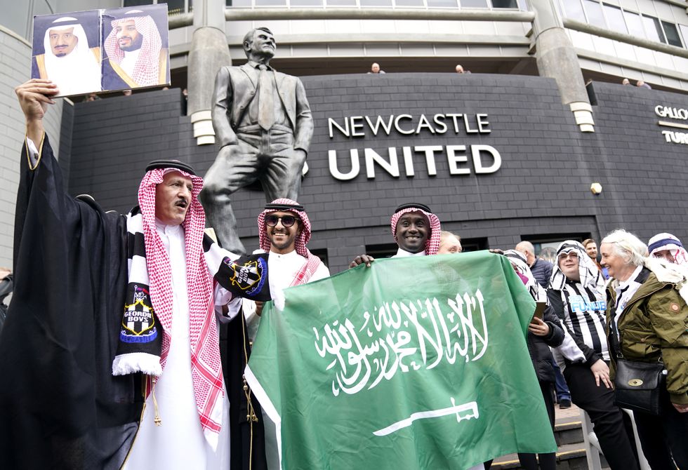 Newcastle United fans outside the stadium hold up a Saudi Arabia flag ahead of a Premier League match at St. James' Park.