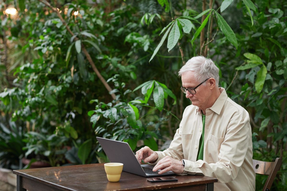 Older person looking at laptop while sitting outside in garden