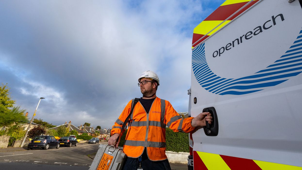 openreach engineer stands in a high-vis jacket with a box of tools outside of his van