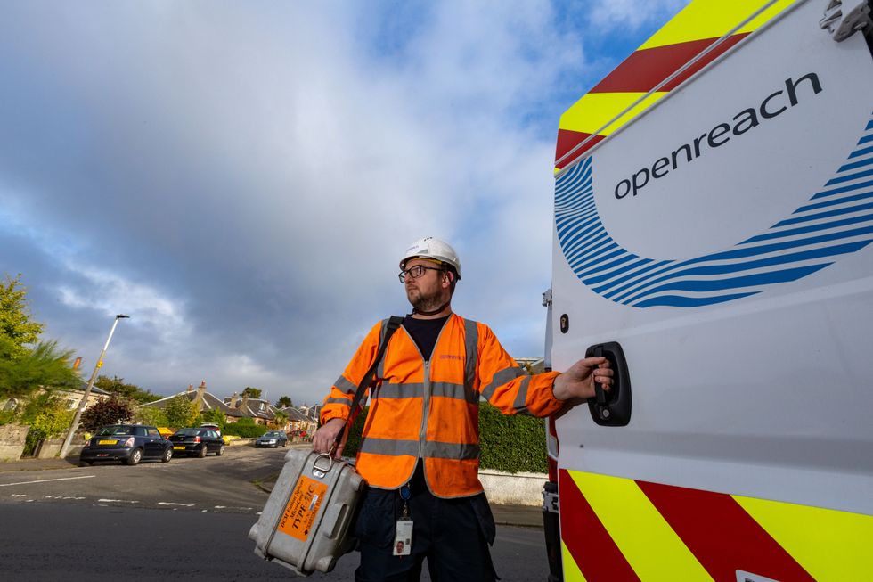 openreach engineer stands in a high-vis jacket with a box of tools outside of his van