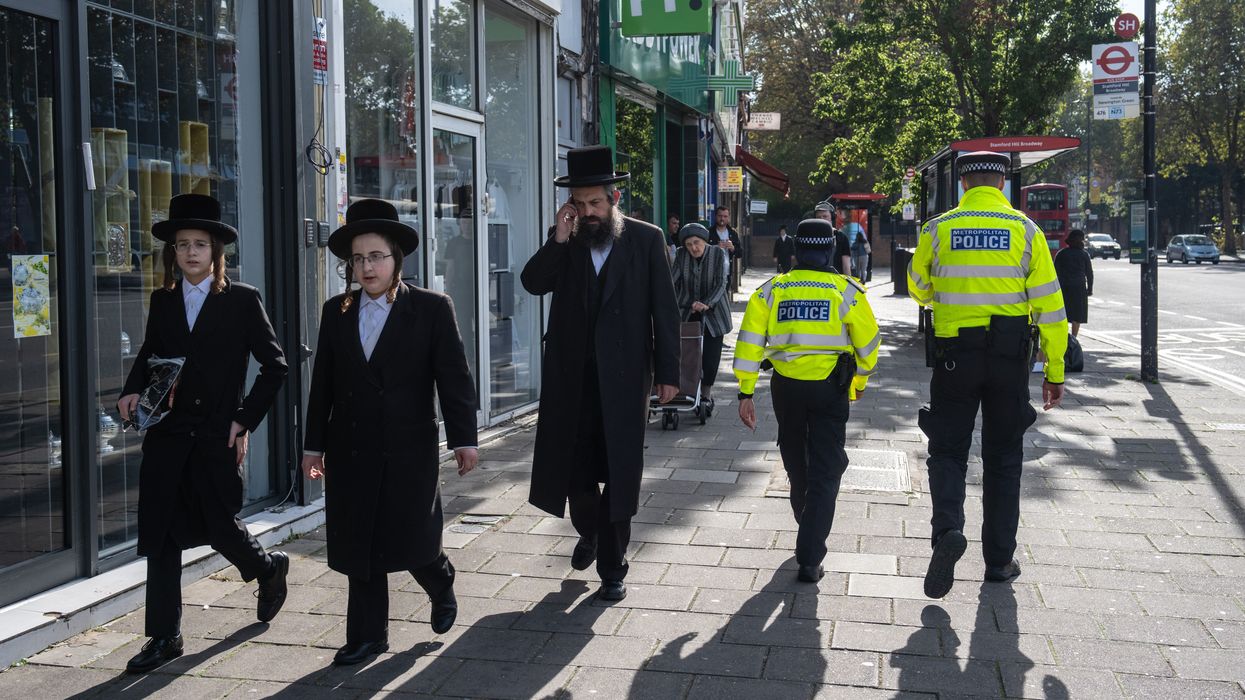 Orthodox Jewish men pass police officers as they patrol around Stamford Hill