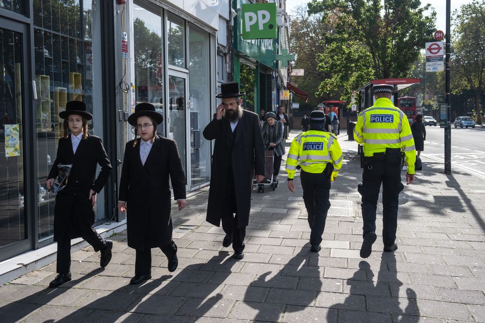 Orthodox Jewish men pass police officers as they patrol around Stamford Hill