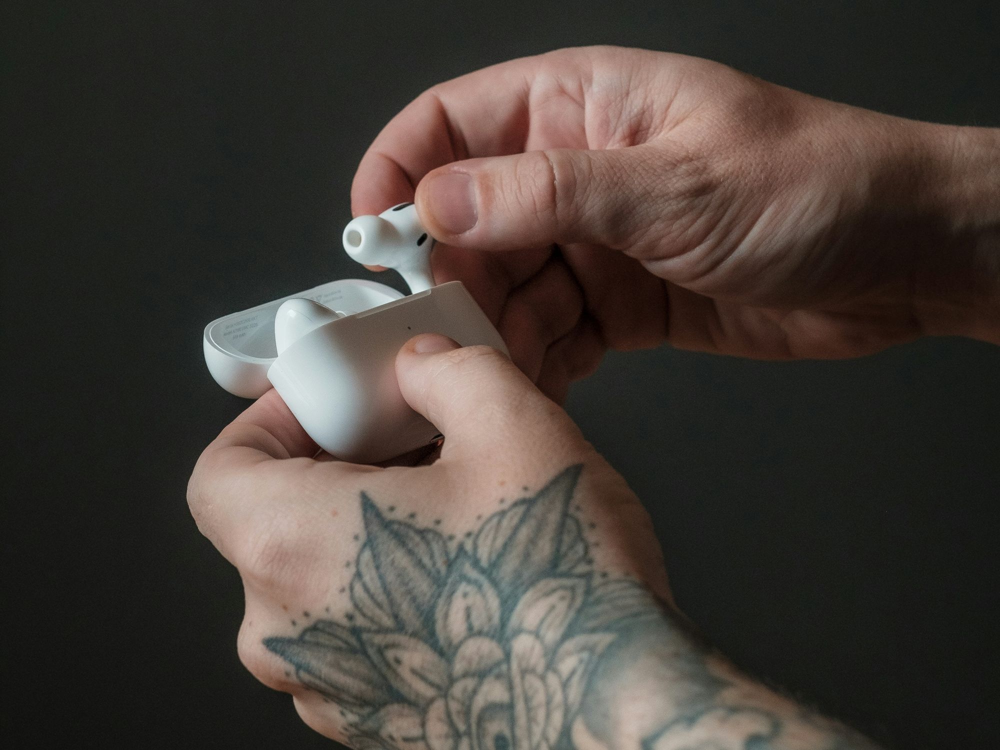 pair of hands with tattoos on the arms open up the airpods pro charging case