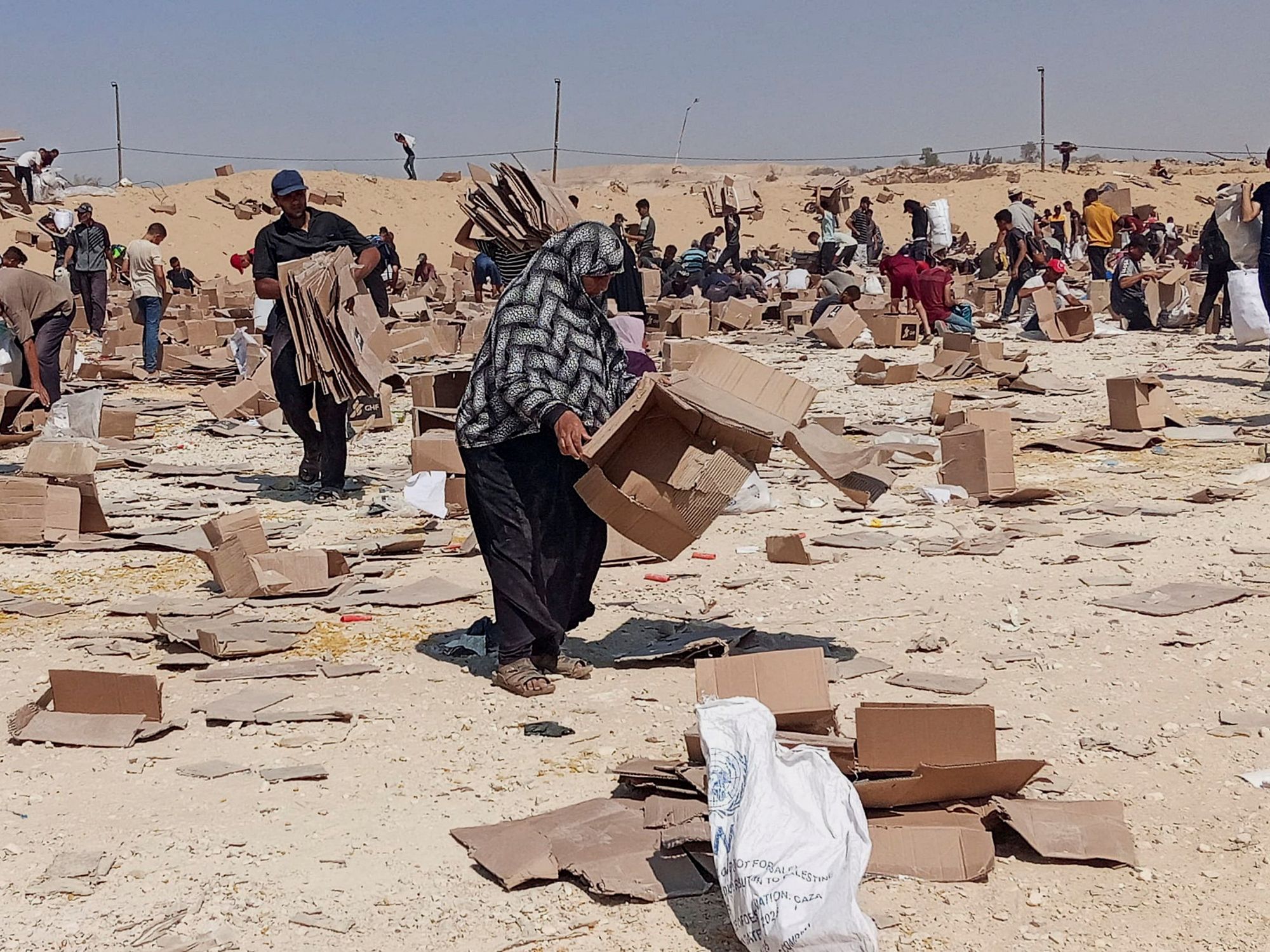 Palestinians gather to collect what remains of relief supplies from a GHF site