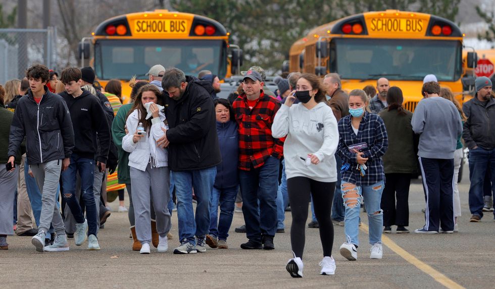 Parents walk away with their kids from the Meijer's parking lot where many students gathered following an active shooter situation at Oxford High School in Oxford, Michigan
