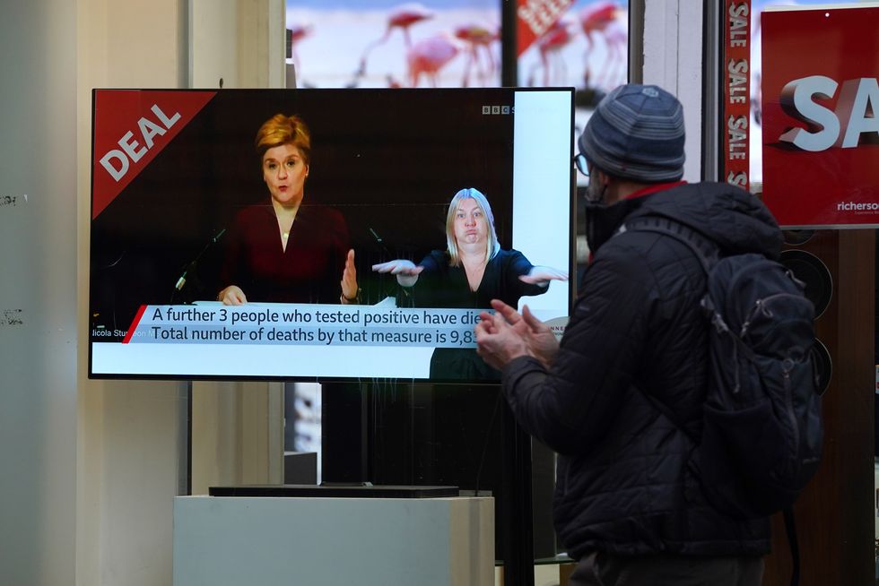 Passers-by look at a tv screen in a Glasgow shop showing First Minister Nicola Sturgeon making a Covid-19 statement during a virtual sitting of the Scottish Parliament. Picture date: Wednesday December 29, 2021.