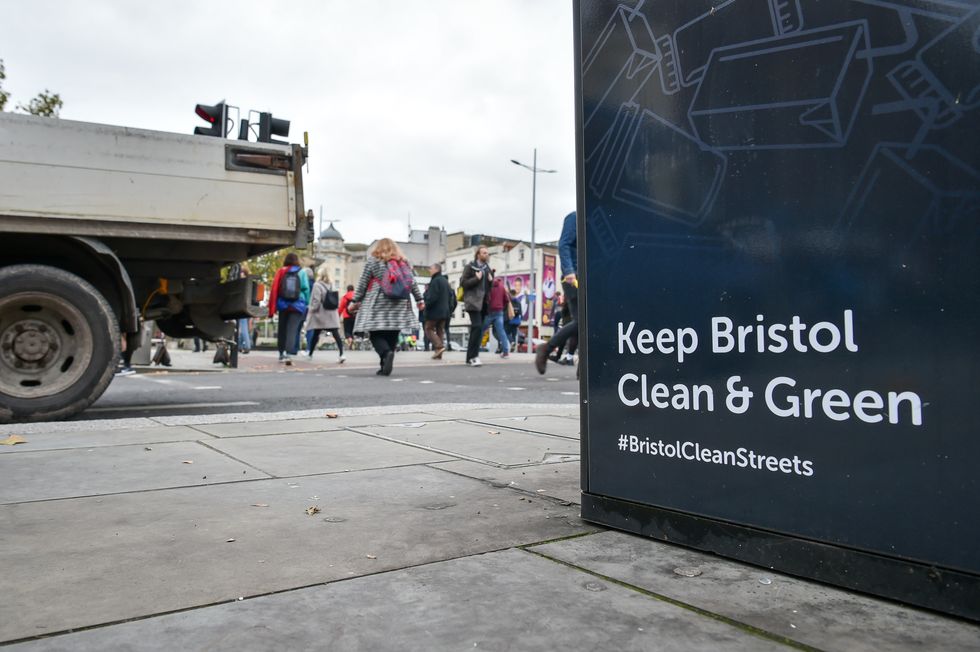 Pedestrians cross behind a commercial vehicle on Baldwin Street in Bristol City centre