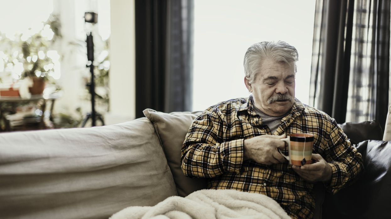 Pensioner holds mug and sits under blanket on sofa