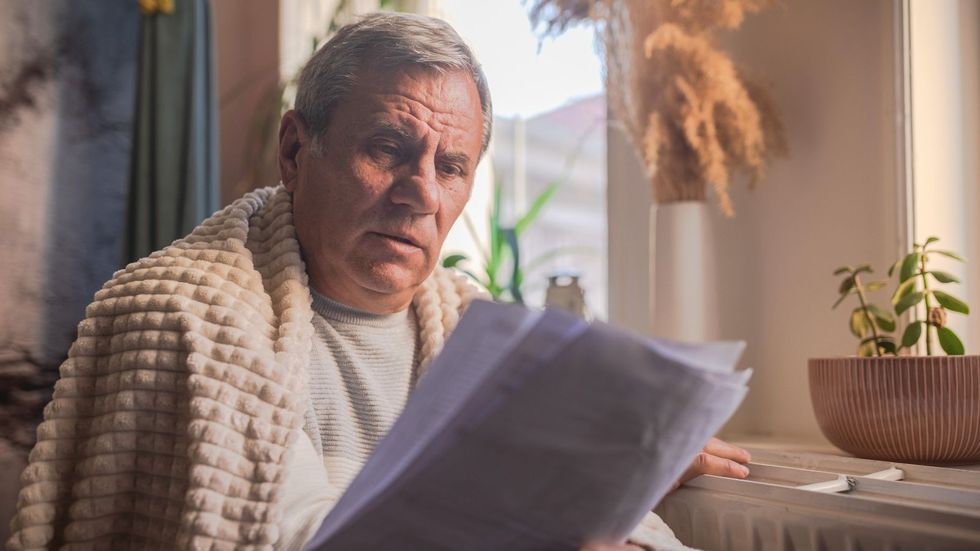 Pensioner in blanket looks at heating bill and energy statement