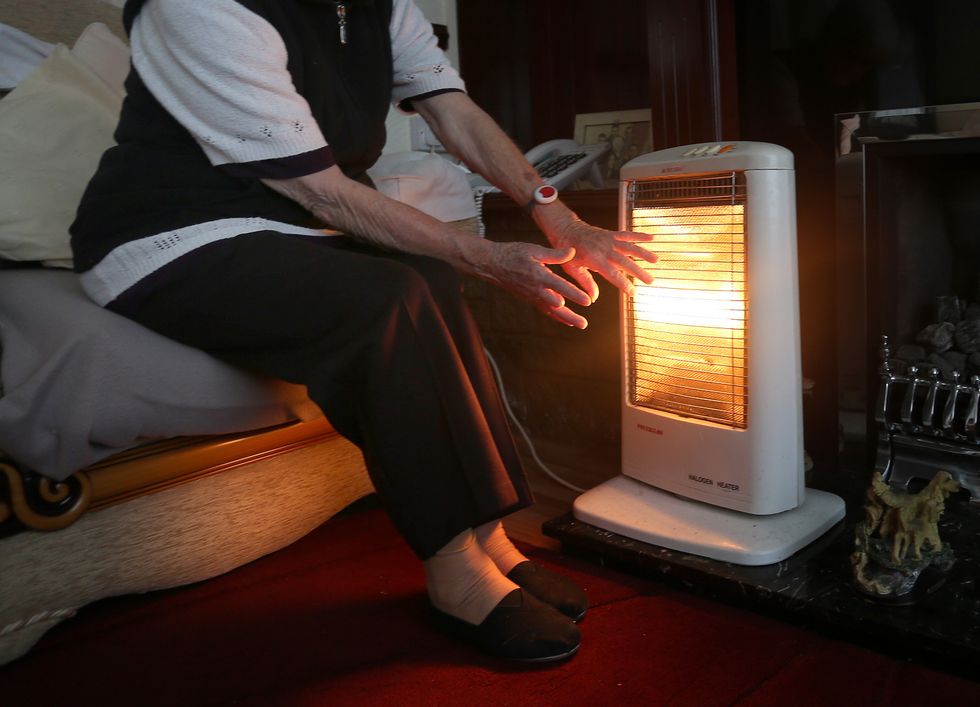 Pensioner keeps warm beside a heater