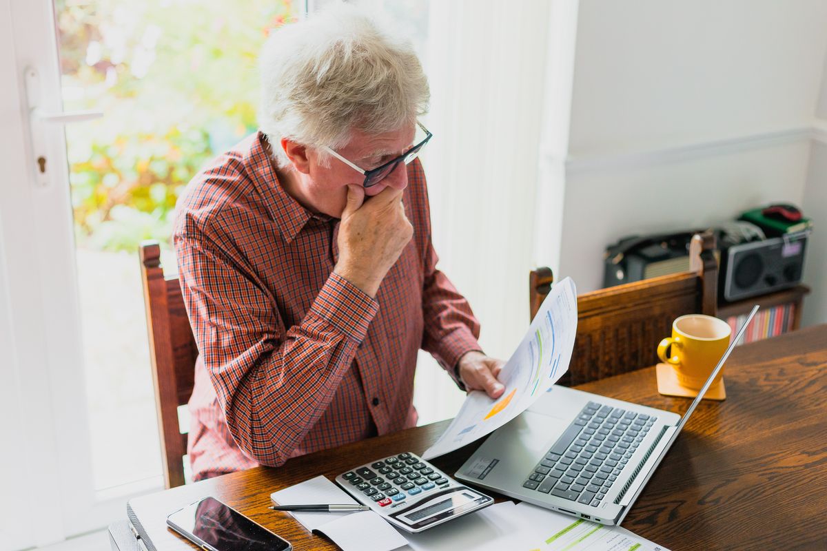 Pensioner looks at finances at desk with calculator and laptop