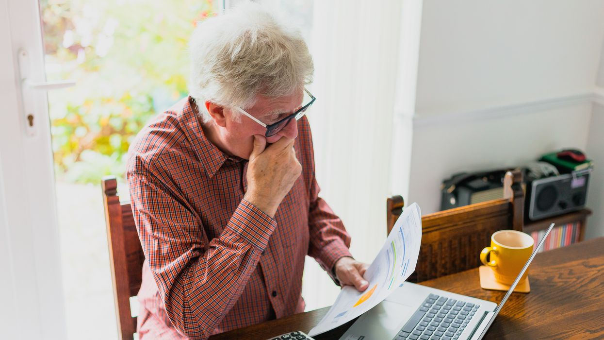 Pensioner looks at finances at desk with calculator and laptop