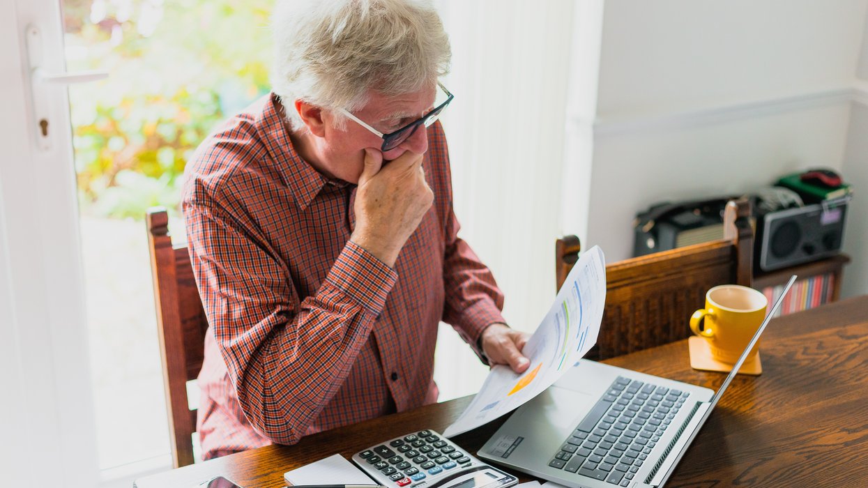 Pensioner looks at finances at desk with calculator and laptop