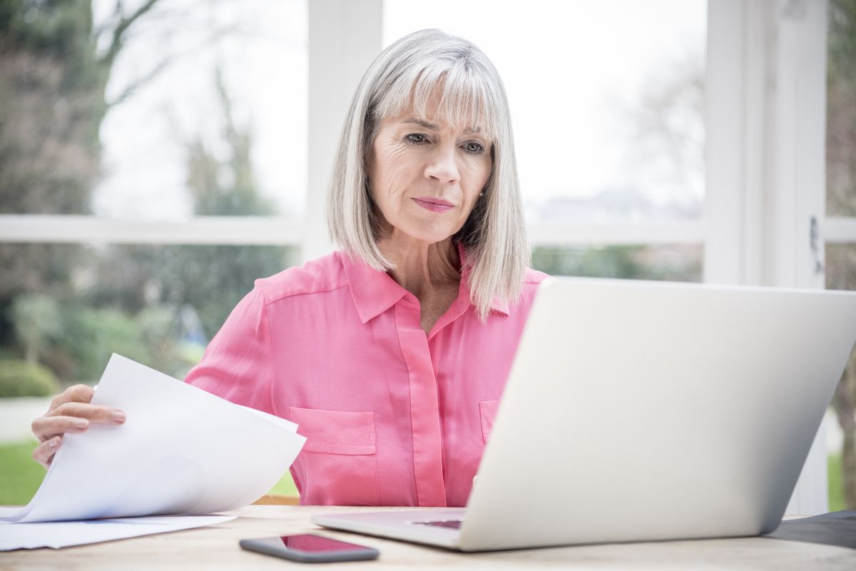 Pensioner looks at laptop with document in hand