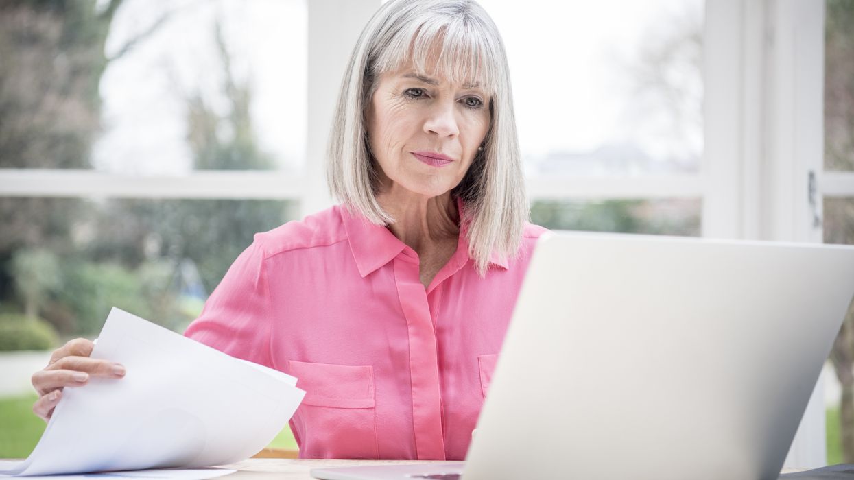 Pensioner looks at laptop with document in hand