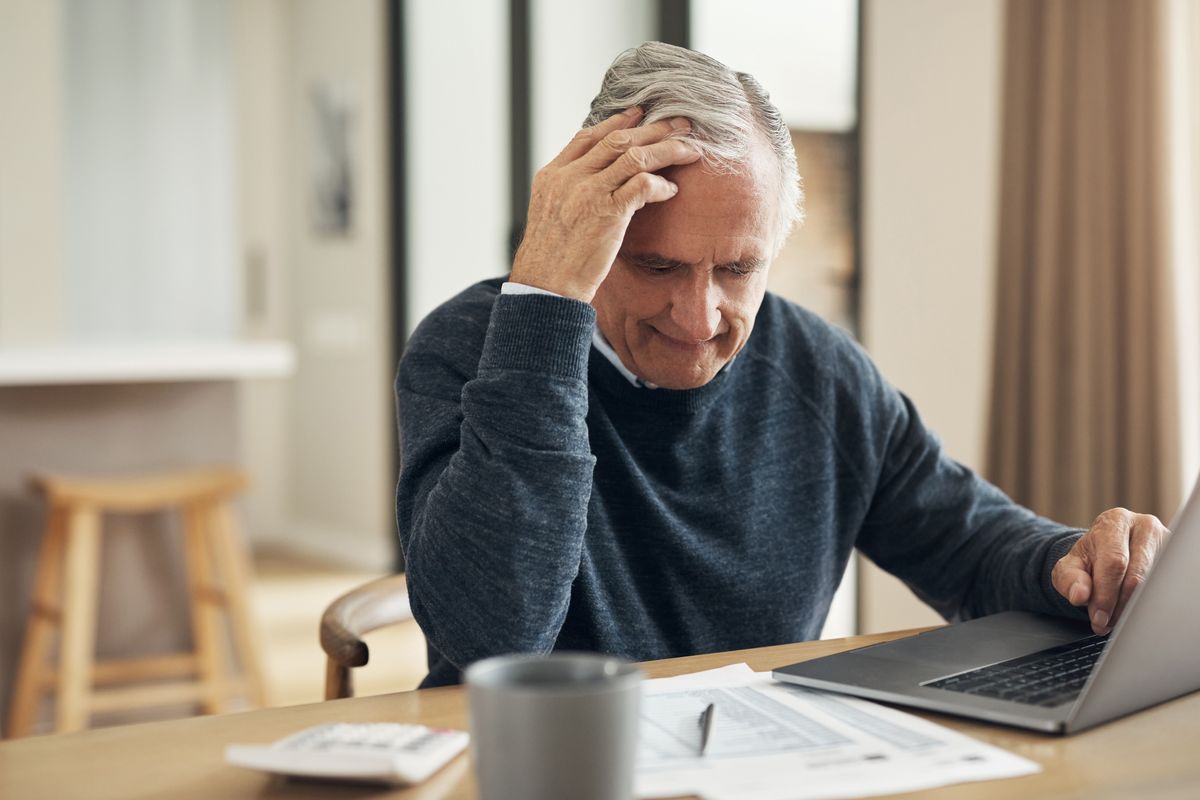 Pensioner looks worried at document beside laptop