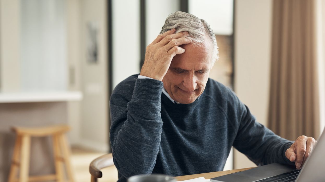 Pensioner looks worried at document beside laptop