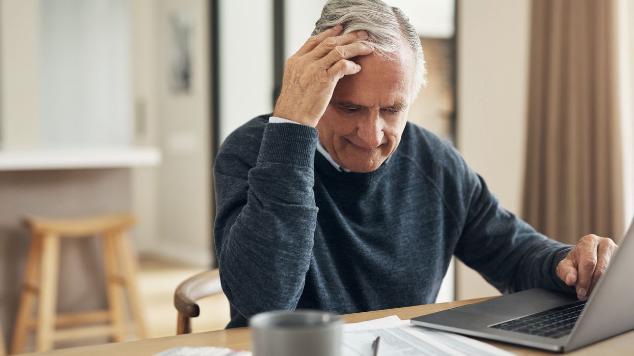 Pensioner looks worried at document beside laptop