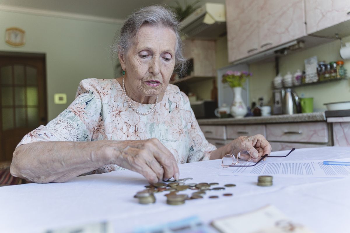 Pensioner looks worried while counting money at kitchen table
