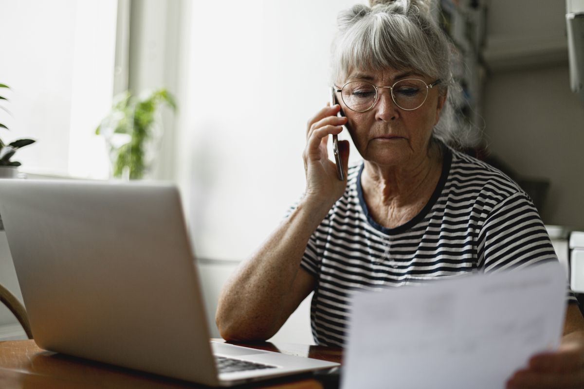 Pensioner on phone with laptop looking at letter