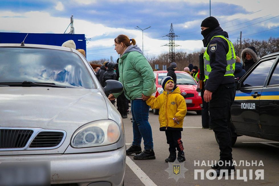 People fleeing from Mariupol amid Russia's invasion of Ukraine stand next to a police officer, in the Zaporizhzhia region.