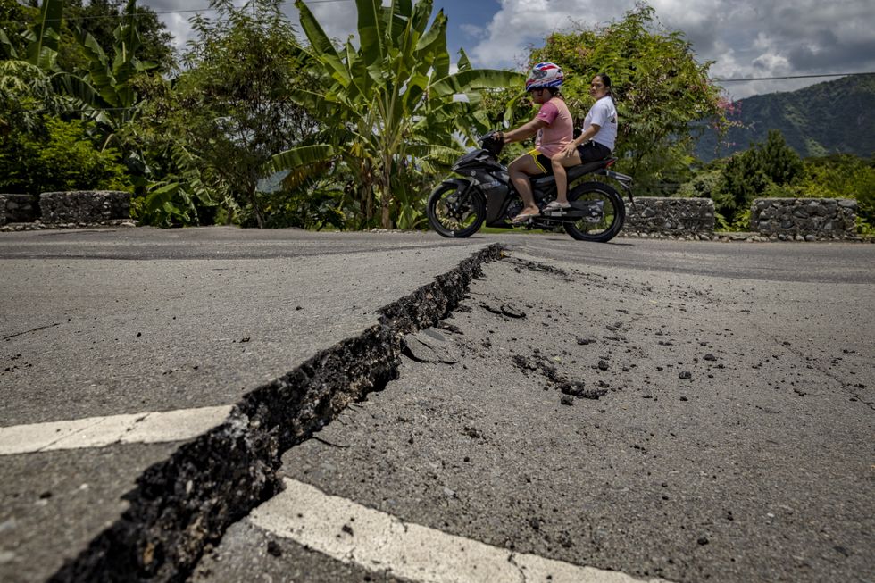People on a motorbike ride over a cracked road following a magnitude 7.0 earthquake