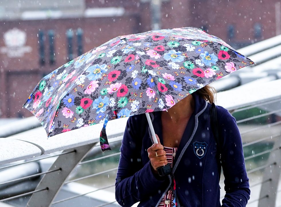 People on the Millennium Bridge in London during a rain shower. The capital saw nearly a month's worth of rainfall on Sunday with homes, roads and Tube stations flooded, while a flooded hospital cancelled all surgery and outpatient appointments on Monday due to the heavy rain. Picture date: Tuesday July 27, 2021.