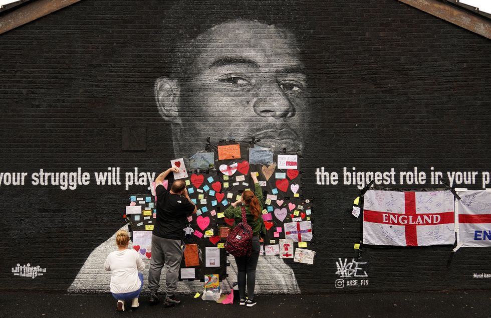 People place messages of support on top of bin liners that were taped over offensive wording on the mural of Manchester United striker and England player Marcus Rashford on the wall of the Coffee House Cafe on Copson Street, Withington, which appeared vandalised the morning after the England football team lost the UEFA Euro 2021 final. Picture date: Monday July 12, 2021.