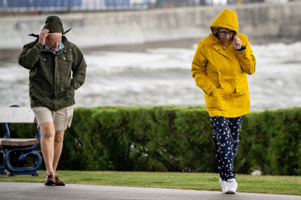 People pull down their hoods to shelter from the wind as they walk along the sea front in Porthcawl, Wales, after winds of up to 75mph lashed parts of the South West as Storm Evert hit the UK on Thursday and Friday.