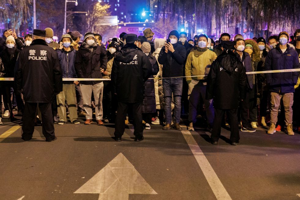 People stand behind a police cordon as they watch a protest over coronavirus disease (COVID-19) restrictions, following a commemoration of the victims of a fire in Urumqi, as outbreaks of COVID-19 continue, in Beijing, China, November 27, 2022. REUTERS/Thomas Peter