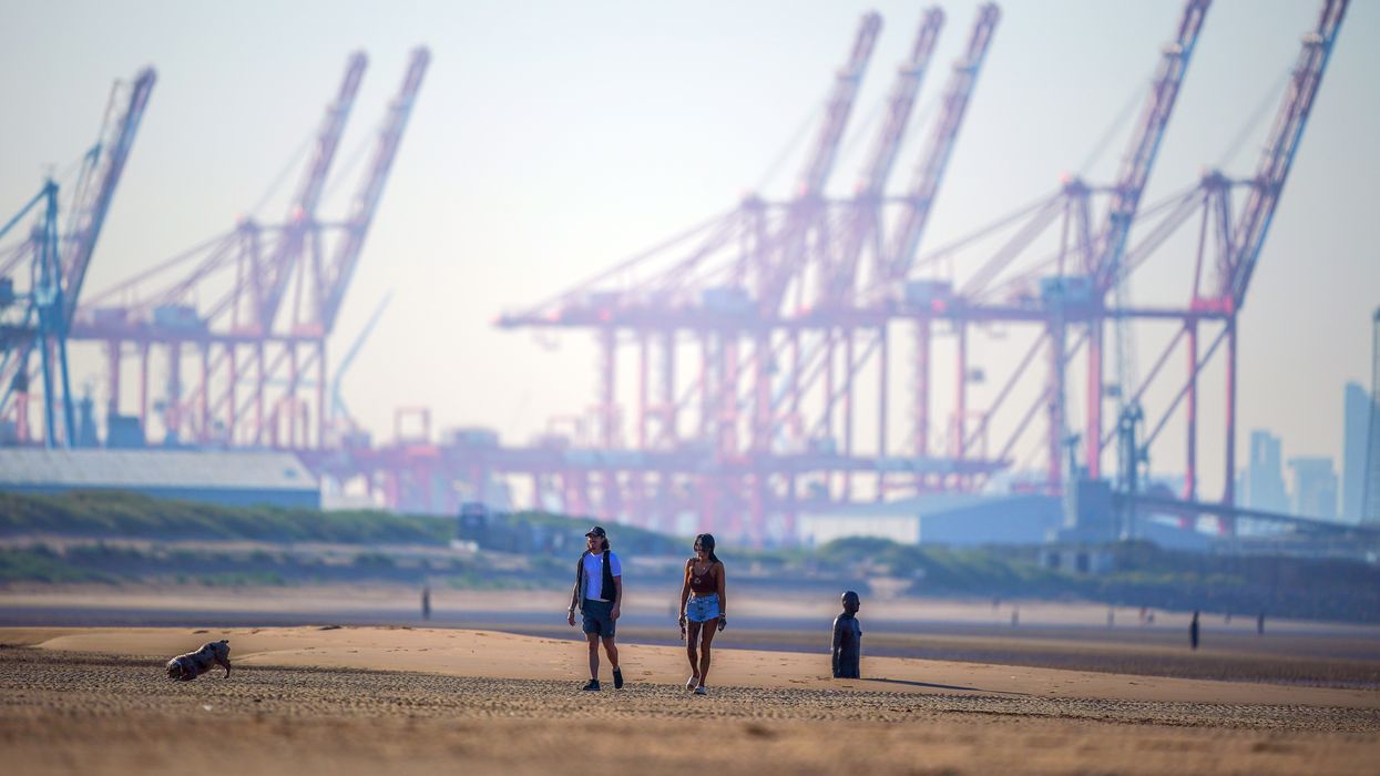 People walk a dog along the beach at Crosby