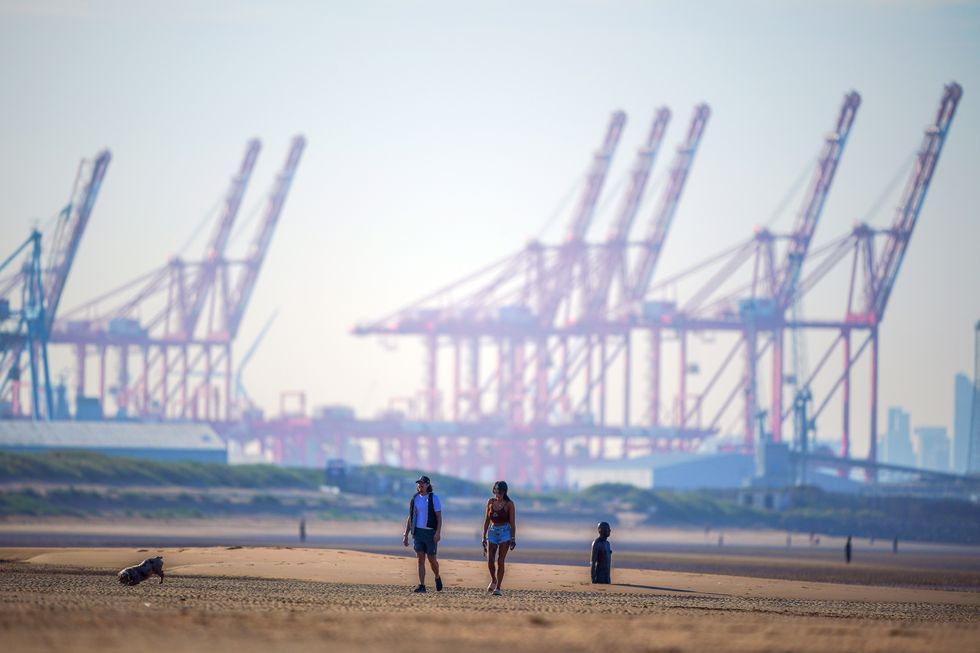 People walk a dog along the beach at Crosby