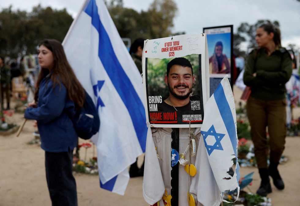 People walk near a poster depicting a hostage Omer Wenkert, at the site of the Nova festival where party goers were killed and kidnapped\u200b